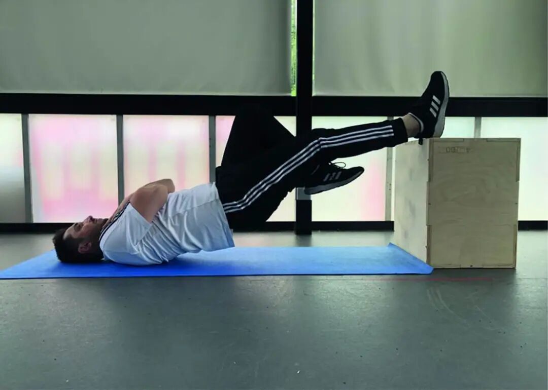 Single Leg Hamstring Bridge (SLHB) test
Participants were asked to perform movements by touching the ground by their bottom and reach 0⁰ of hip extension by lifting their bottom respectively and without resting with the help of a 60-cm high box. The other leg was in a vertical position as inactive and stationary to eliminate any momentums that might be provided by swinging the leg. Participants were advised to aim to perform as much as they could repeat the same movement until failure. The individual pictured in Fig 4 has provided written informed consent (as outlined in PLOS consent form) to publish their image alongside the manuscript.